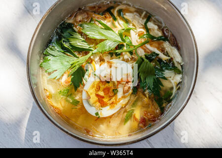 Soto ayam, une soupe de poulet jaune avec oeuf dur, persil et bawang goreng (oignon frit). Une cuisine indonésienne. Banque D'Images