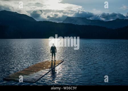 Silhouette homme debout sur le radeau en bois sur le lac bleu. Cloudy Mountain dans le dos avec la lumière du soir en nature paysage Banque D'Images