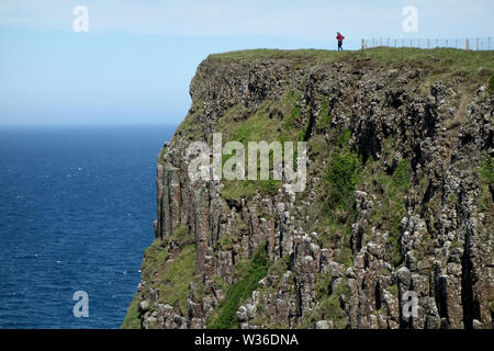 Homme marchant au-dessus des falaises de Benbane Head sur le Giant's Causeway chemin côtier, comté d'Antrim, en Irlande du Nord, Royaume-Uni Banque D'Images