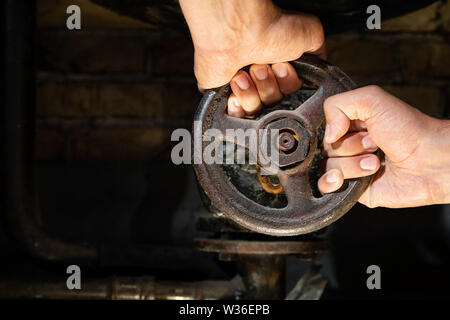 Mans mains essayant de tourner la vanne rouillée sur chaufferie tuyaux. Vieille chaudière chauffage production de métaux et de la livrer à la maison par l'entremise de pipelines Banque D'Images