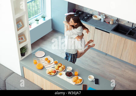 Dark-haired mari heureux de lever son épouse dans la cuisine Banque D'Images