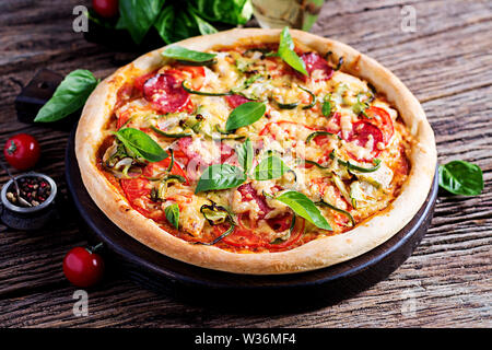 Pizza italienne avec du poulet, de salami, de courgettes, tomates et fines herbes sur fond de bois vintage. La cuisine Italienne Banque D'Images