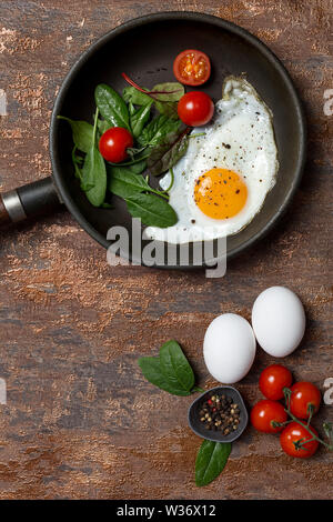 Pan avec petit-déjeuner d'œuf frit, tomates cerises, roquette et épinards sur fond brun. Concept de petit-déjeuner sain avec des légumes. Voir ci-dessus, f Banque D'Images