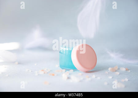 Liquide essentiel dans un pot cosmétique sur un fond bleu avec des plumes blanches des maquettes Banque D'Images