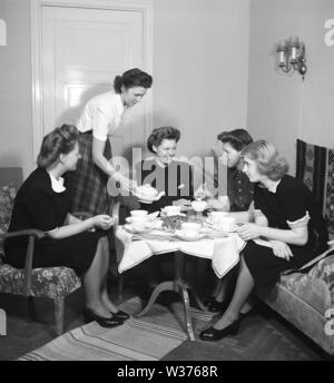 Temps de thé en 1940s. Un groupe de jeunes femmes s'amusent à se fika autour d'une table avec des tasses à thé et des gâteaux. L'hôtesse verse le thé dans une jolie bouilloire en porcelaine. En 1940s, lorsque seules les femmes se sont rencontrées et ont bu du thé ou du café, était un événement social. Ils pouvaient s'asseoir et discuter, échanger des potins et des nouvelles sans l'implication de leurs hommes ou de leurs enfants. Suède 1945 Kristoffersson Réf. M74-2 Banque D'Images