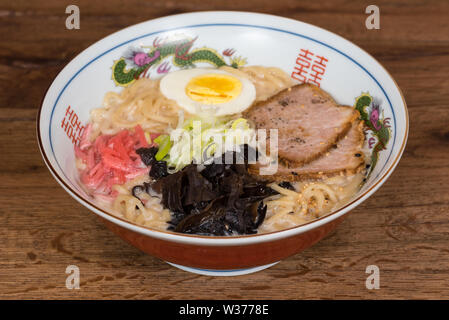 Tonkotsu Ramen au porc, lait de soja, bouillon de porc, les champignons noirs, les oeufs, les oignons, servi dans un bol en bois foncé, fond de table Banque D'Images