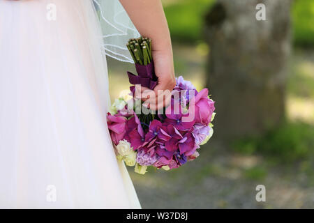 La mariée tient un bouquet de mariage dans sa main contre l'arrière-plan d'une robe blanche. Banque D'Images