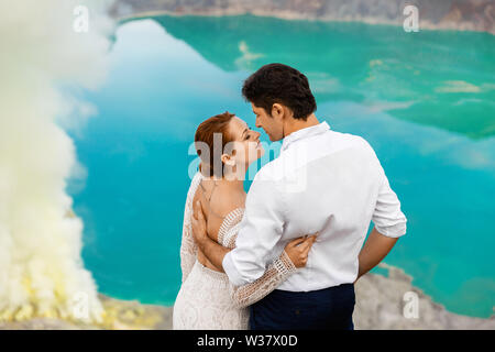 Bride and Groom hugging sur fond d'un lac vert et de fumée volcanique dans le cratère du volcan Banque D'Images