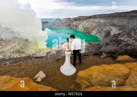 Mariée et le marié hug debout dans le cratère d'un volcan sur un fond de lac vert et acide sulfurique de fumée volcanique Banque D'Images