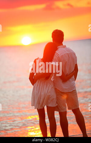 Lune de miel romantique dans l'amour à la plage au coucher du soleil. Young woman hugging bénéficiant d'ocean sunset lors des voyages vacances escapade. Couple Interracial, Asian Woman, man. Banque D'Images