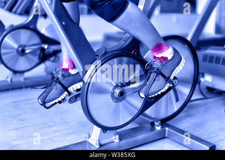 Blessures sportives - douleur à la cheville au cours de la formation sur spinning bike au sport. Libre de jambes de l'athlète féminine à l'aide de location la machine au centre de remise en forme en bleu filtre monochromatique. Banque D'Images