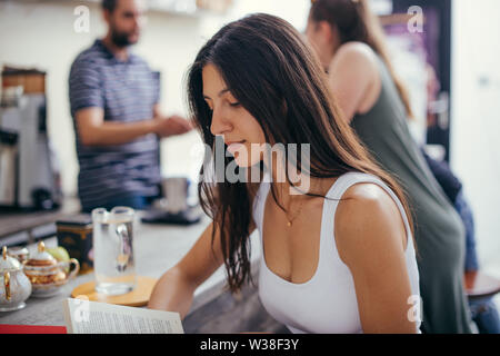 Portrait of young female reading book en étant debout avec barista travaillant derrière le comptoir préparer des consommations Banque D'Images