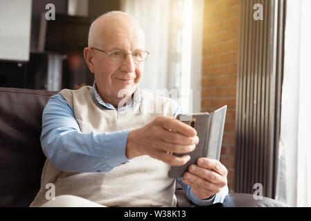 Man à l'aide d'un smartphone et souriant alors qu'il était assis sur la table à la maison. Banque D'Images