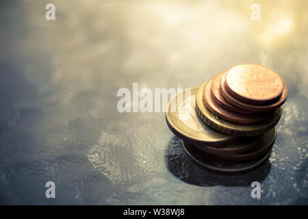 Une pile de pièces en euro brillant sur une table en verre avec lumière du soleil chaud, soft focus sélectif Banque D'Images