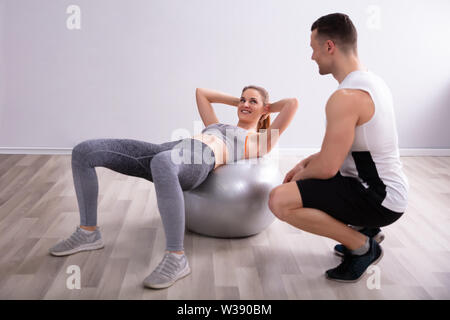 Happy young woman doing Entraînement avec Fitness Ball en face de formateur Banque D'Images