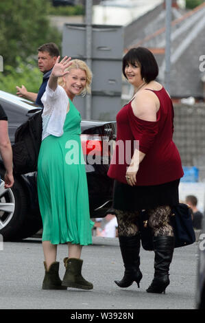 Barry, Royaume-Uni. Le 13 juillet, 2019. (L-R) Joanna Page qui joue 'Stacey' et co-scénariste Ruth Jones qui joue 'Nesa' vague de spectateurs lors d'une pause dans le tournage de la comédie de la BBC Gavin & Stacey dans Trinity Street, Barry, Galles du Sud. Credit : Mark Lewis/Alamy Live News Banque D'Images