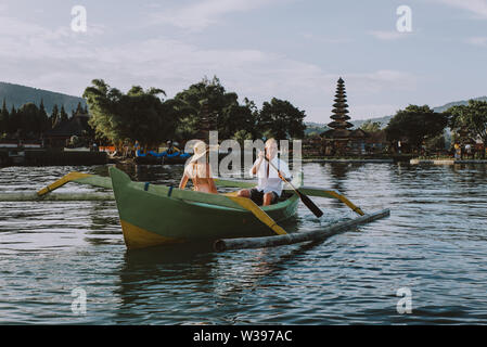 Jeune beau couple pagayer sur un bateau en bois à Pura Ulun Danu Bratan, Bali - Touristes explorer Bali Banque D'Images