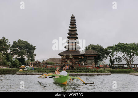 Jeune beau couple pagayer sur un bateau en bois à Pura Ulun Danu Bratan, Bali - Touristes explorer Bali Banque D'Images