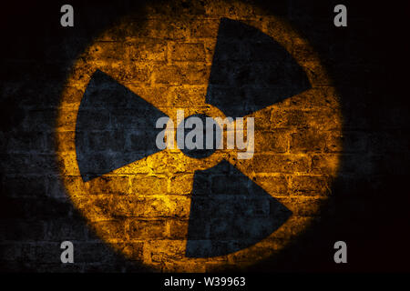 L'énergie nucléaire (rayonnements radioactifs rayonnement atomique) rond jaune forme de symbole peint sur la brique de béton wall texture fond sombre. Nuclea Banque D'Images