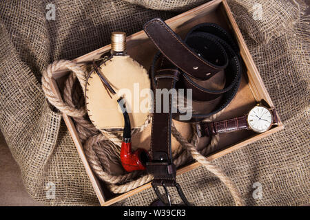 Accessoires pour hommes avec ceinture en cuir marron, lunettes, montre, pipe et une bouteille de parfum sur fond rustique. Vue d'en haut. Banque D'Images