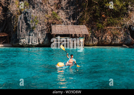 La pagaie touristiques sur un transparent kajak sur une plage tropicale avec palmiers et l'eau bleue - Coron, Philippines Banque D'Images