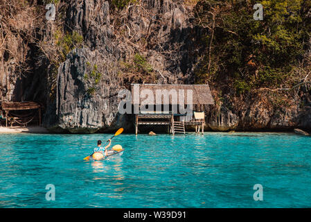 La pagaie touristiques sur un transparent kajak sur une plage tropicale avec palmiers et l'eau bleue - Coron, Philippines Banque D'Images