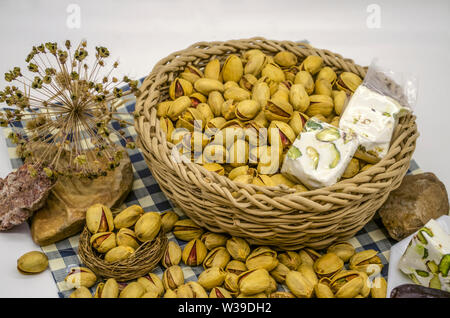 Des pierres et des fleurs séchées à côté de fried pistaches, kakis et nougat dans un panier en osier et une plaque blanche sur papier de carrés bleus Banque D'Images