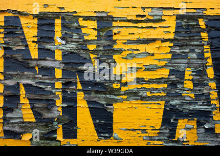Gros plan d'une surface peinte altérée et écaillée avec des lettres jaunes et noires décolorées sur fond de bois détérioré Banque D'Images