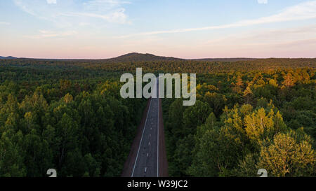 Vue du haut de la route de terre et le vert des forêts de printemps dans des couleurs au coucher du soleil. Beau paysage de l'air, photographie du bourdon Banque D'Images