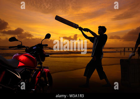 Teenage boy playing cricket sur la plage au crépuscule Banque D'Images