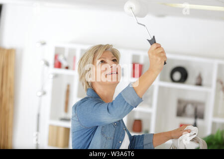 Femme mature en utilisant le rouleau à peindre le plafond Banque D'Images