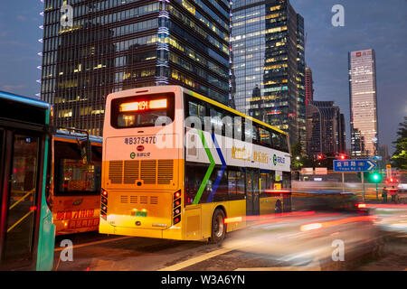 Electric city bus de passer dans la rue d'affaires de Futian Central au crépuscule. Shenzhen, province de Guangdong, en Chine. Banque D'Images