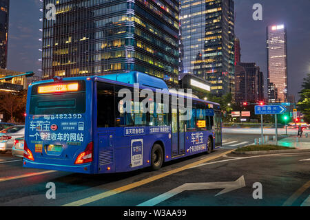 Electric Blue city bus de passer dans la rue d'affaires de Futian Central au crépuscule. Shenzhen, province de Guangdong, en Chine. Banque D'Images