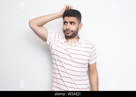 Portrait de query beau jeune homme barbu en t-shirt à rayures comité permanent se gratte la tête, rabotage et penser à quelque chose. Piscine studio shot Banque D'Images