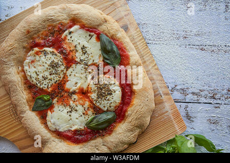 Des pizzas au four à la maison. La farine de blé entier, de la sauce tomate, mozzarella et padano fromages, tomates cerises, origan et l'ail. Banque D'Images