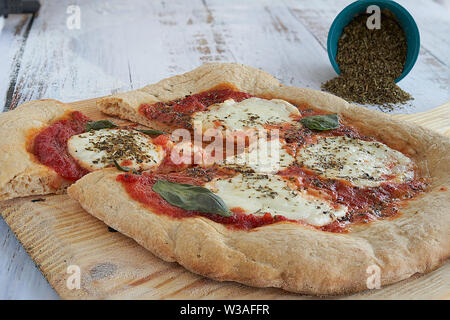 Des pizzas au four à la maison. La farine de blé entier, de la sauce tomate, mozzarella et padano fromages, tomates cerises, origan et l'ail. Banque D'Images