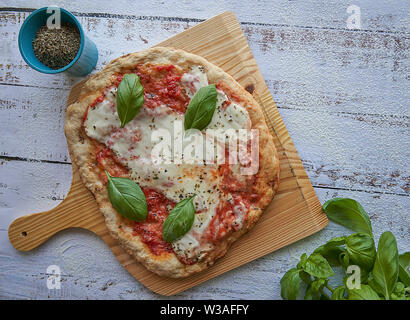 Des pizzas au four à la maison. La farine de blé entier, de la sauce tomate, mozzarella et padano fromages, tomates cerises, origan et l'ail. Banque D'Images