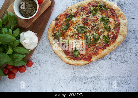 Des pizzas au four à la maison. Sauce tomate, mozzarella et padano fromages, tomates cerises et petits poivrons épicés, l'origan et l'ail. Banque D'Images