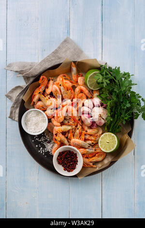 Crevettes crues dans une casserole avec les ingrédients pour la préparation crevettes frites on blue background vue supérieure Banque D'Images