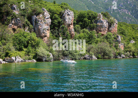 Petit yacht blanc près de la côte rocheuse sur le magnifique lac d'Ohrid, République de Macédoine du Nord Banque D'Images