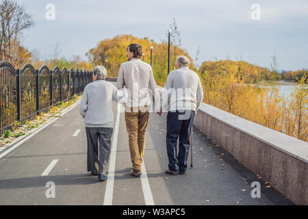 Un couple de personnes âgées des promenades dans le parc avec un homme assistant ou petit-fils adultes. La prise en charge des personnes âgées, le bénévolat Banque D'Images