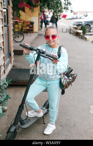 Happy kid dans sunglssses article sur scooter électrique en ville rue Banque D'Images