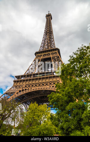 Un faible taux d'angle de vue de la célèbre Tour Eiffel en format portrait. Certains arbres sont couvrant certaines parties de la tour alors que les nuages s'accumulent... Banque D'Images
