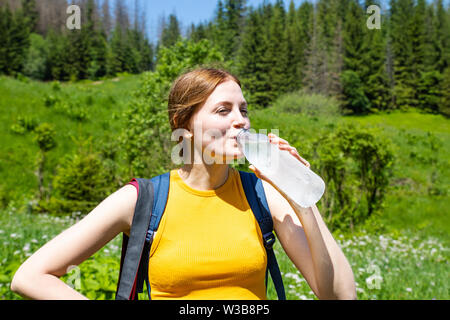 Woman girl in a yellow T-shirt et jeans shorts boire de l'eau dans une bouteille en plastique sur un fond de forêt verte .Femme repose dans le Banque D'Images