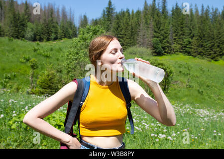 Woman girl in a yellow T-shirt et jeans shorts boire de l'eau dans une bouteille en plastique sur un fond de forêt verte .Femme repose dans le Banque D'Images