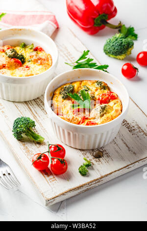 La Frittata avec brocoli dans deux formes de céramique. La Frittata avec brocoli, poivrons doux et tomates en deux formes en céramique pour la cuisson. Omelette italienne w Banque D'Images