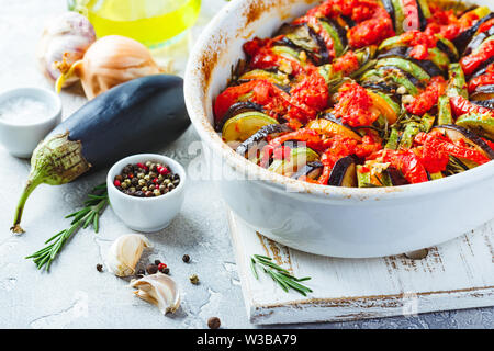 Ratatouille végétarien de aubergines, courgettes, tomates et sauce tomate et poivrons aux herbes en forme de céramique avant la cuisson. Style rustique. Banque D'Images