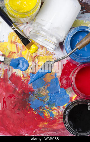 Les bocaux en verre acrylique avec couleurs primaires et une palette sale avec une spatule et brosses Banque D'Images