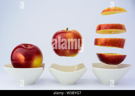 Une pomme rouge ensemble, faire léviter au-dessus d'une tasse et coupé en gros morceaux aussi léviter au-dessus d'une tasse Banque D'Images
