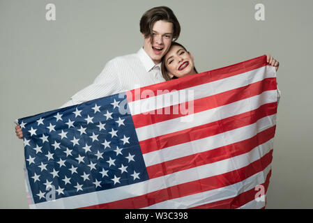 Le couple smiling faces est titulaire d'un drapeau des USA. Guy et fille heureuse avec le drapeau américain, fond gris. Concept d'un voyage à l'étranger. Rêve de visiter quelques Banque D'Images